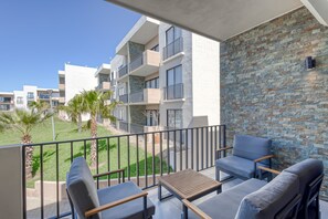 A balcony with outdoor seating, a stone wall, and a view of adjacent buildings. - Bright and Modern Condo w/ Balcony, Shared Pool, A/c, Minutes to Beach & Town (Cabo San Lucas)