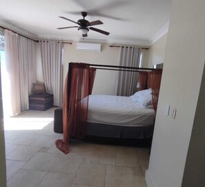 A bedroom with a bed, a ceiling fan, curtains, a window, and a wall-mounted air conditioner.