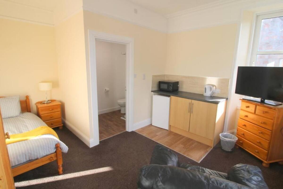 A bedroom with a bed, bedside table, lamp, and a TV.