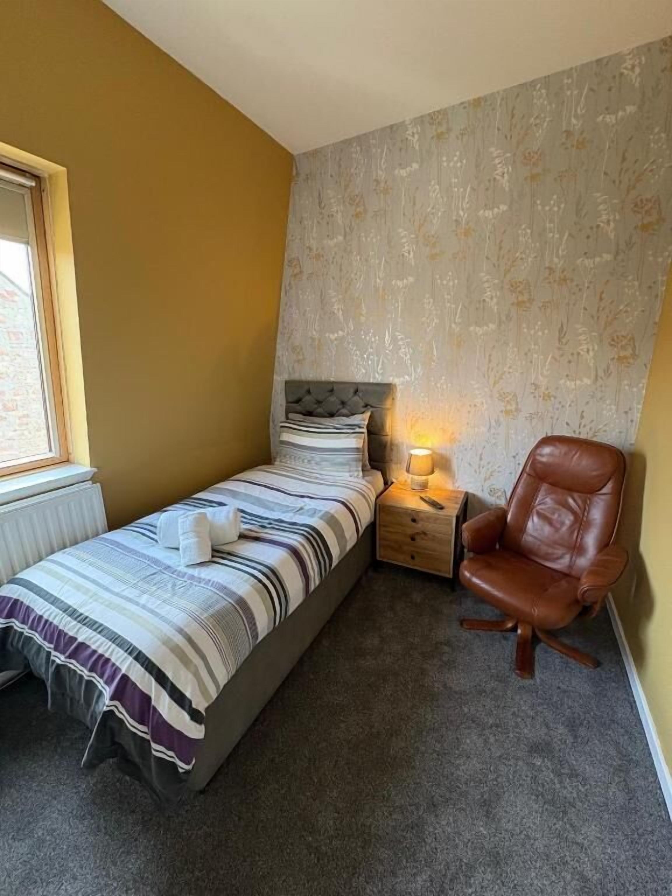Una camera da letto con un letto, una lampada da comodino, una sedia e una finestra.