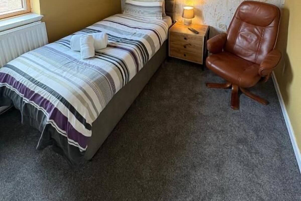 A bedroom with a bed, bedside lamp, chair, and a window.