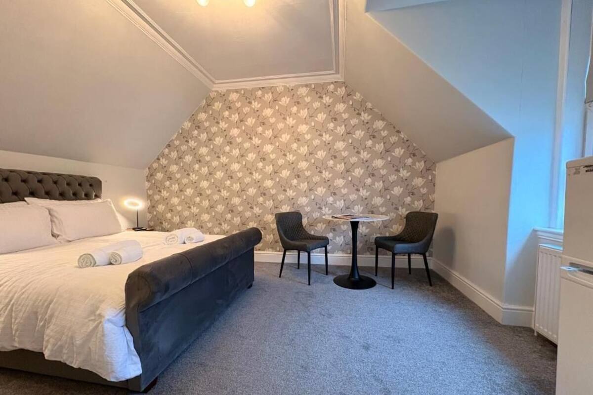 A bedroom with a bed, two chairs, a small table, and a radiator.