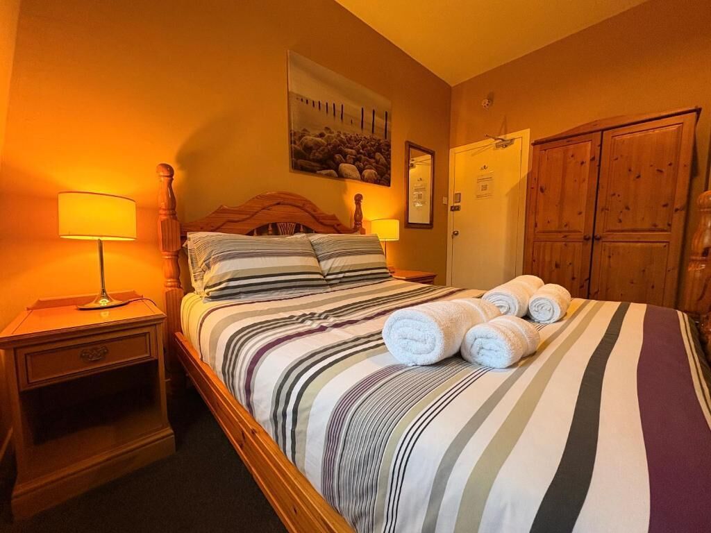Una camera d'albergo con un letto, un comodino, una lampada, un armadio in legno e un quadro appeso al muro.