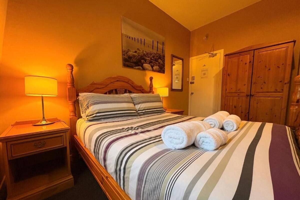 A hotel room with a bed, a nightstand, a lamp, a wooden wardrobe, and a painting on the wall.