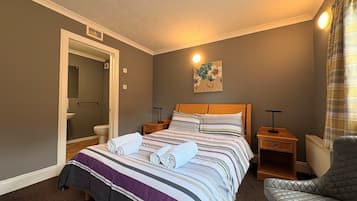 Hotellihuone, jossa on sänky, tuoli, taulu, yöpöytä ja kylpyhuoneen ovi.