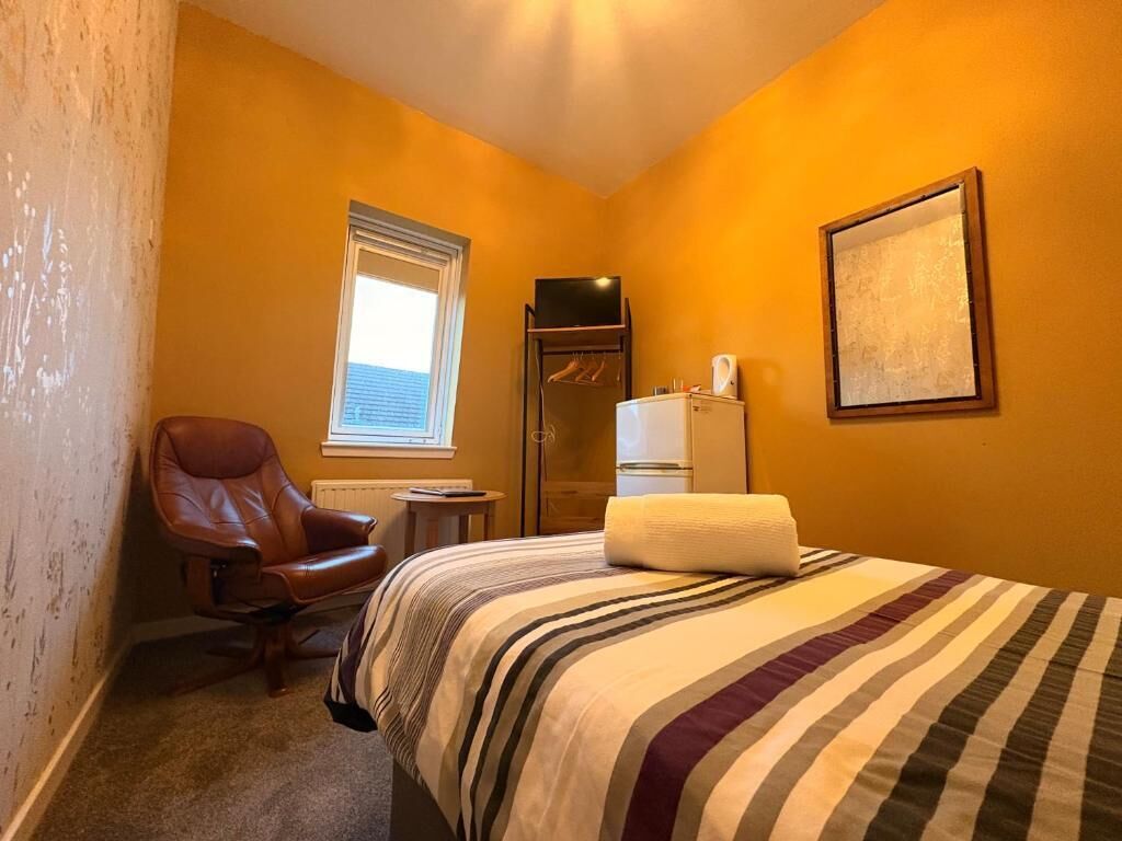 Una camera d'albergo con un letto, una sedia, una finestra, un termosifone e un televisore.
