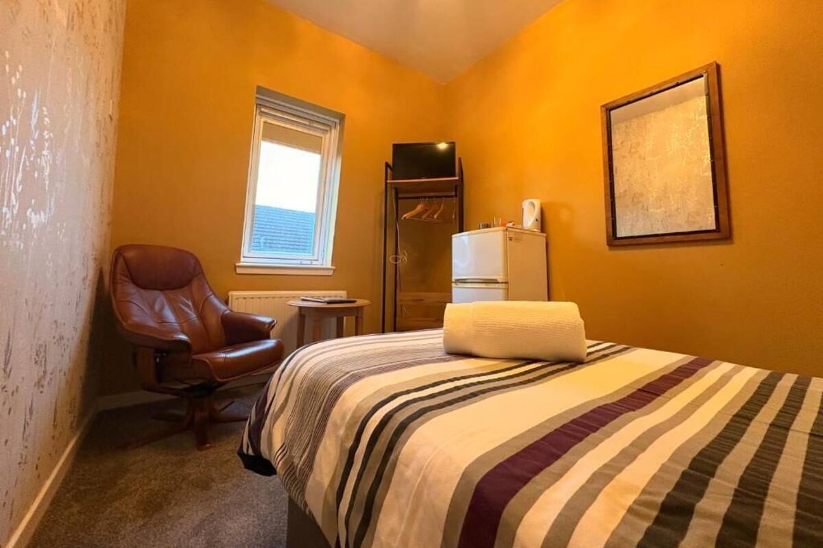 A hotel room with a bed, a chair, a window, a radiator, and a television.