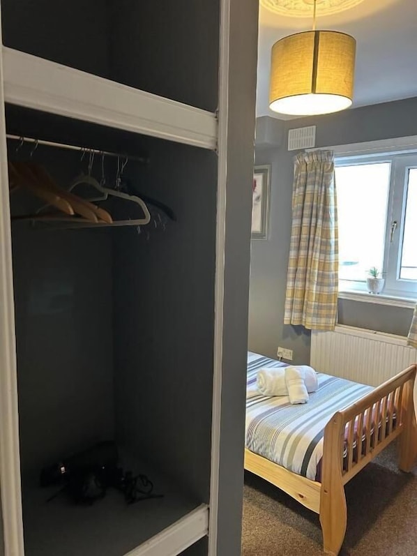 Une chambre à coucher avec un lit, une armoire, une fenêtre avec des rideaux et une lampe suspendue.
