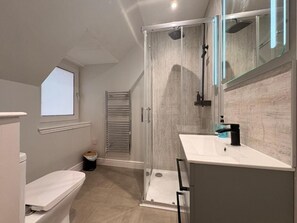 Un bagno moderno con cabina doccia in vetro, un lavandino bianco e una finestra sopra il water.