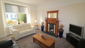 A living room with a white sofa, a fireplace, a television, and a coffee table. - Winmar Guesthouse (Inverness)