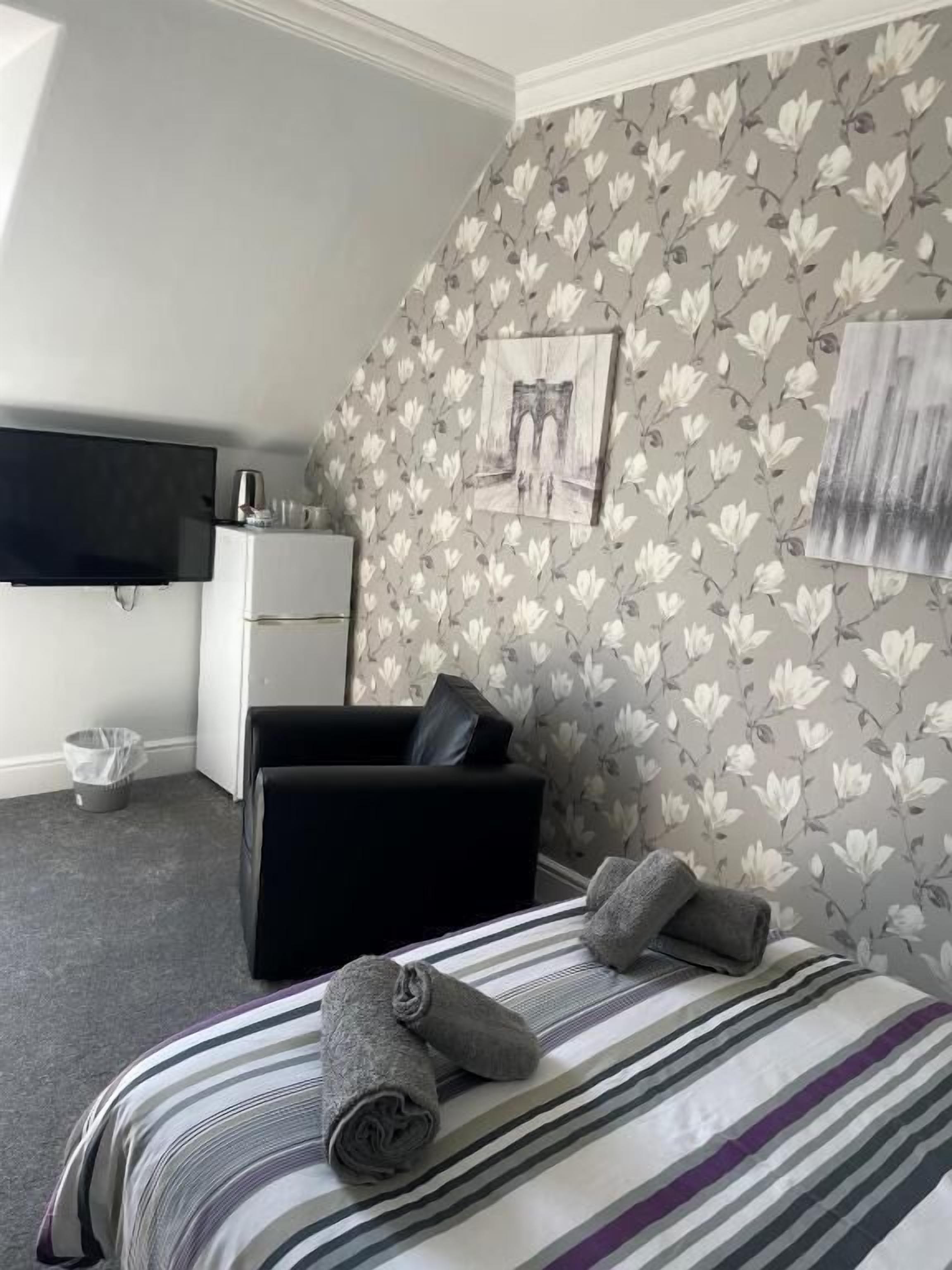 Una camera d'albergo con un letto, un divano nero, una televisione a schermo piatto e un tavolino con un bollitore.