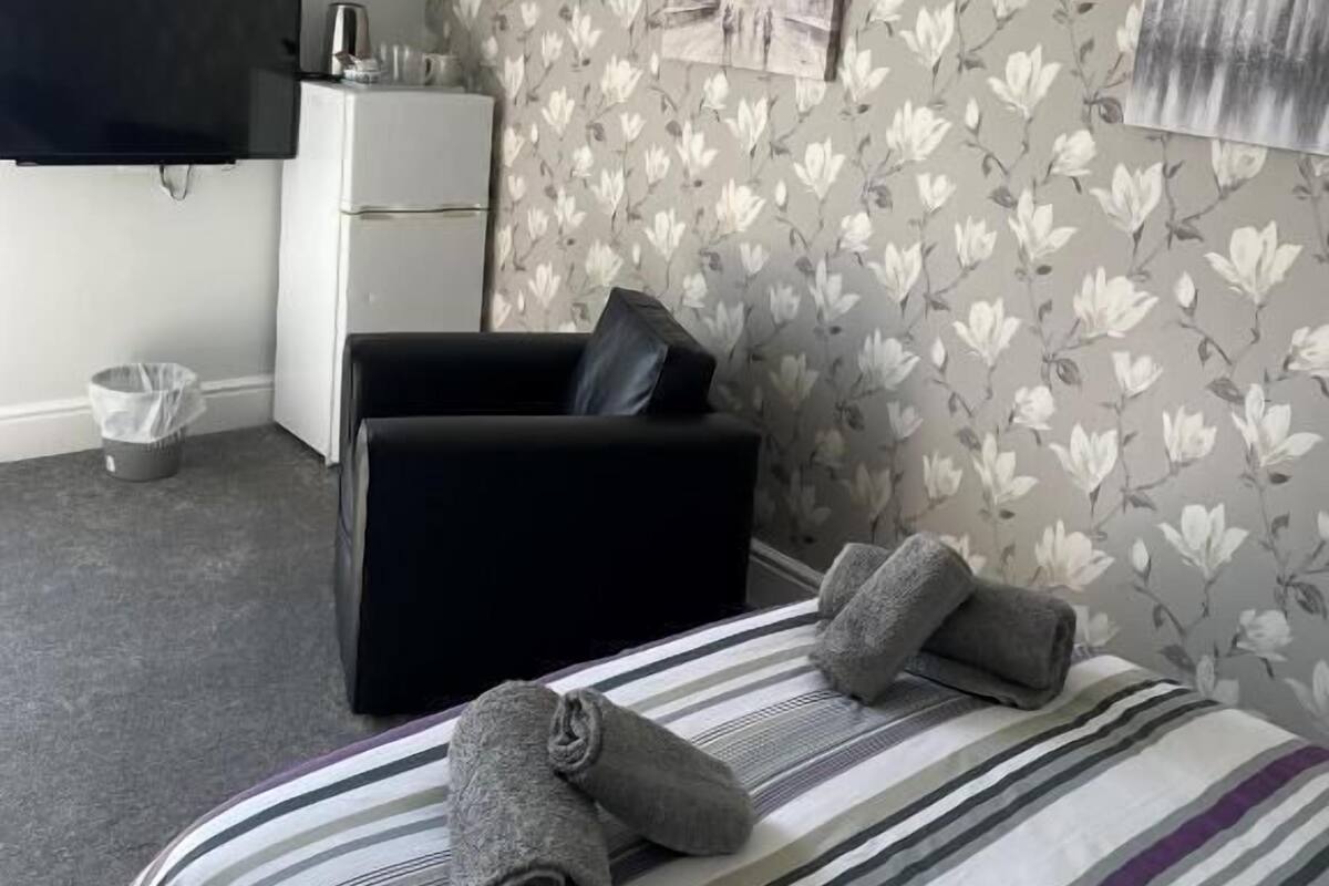 A hotel room with a bed, a black sofa, a flat-screen TV, and a small table with a kettle.