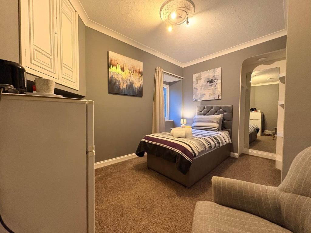 Una camera da letto con un letto, una sedia, una cassettiera e un quadro appeso al muro.
