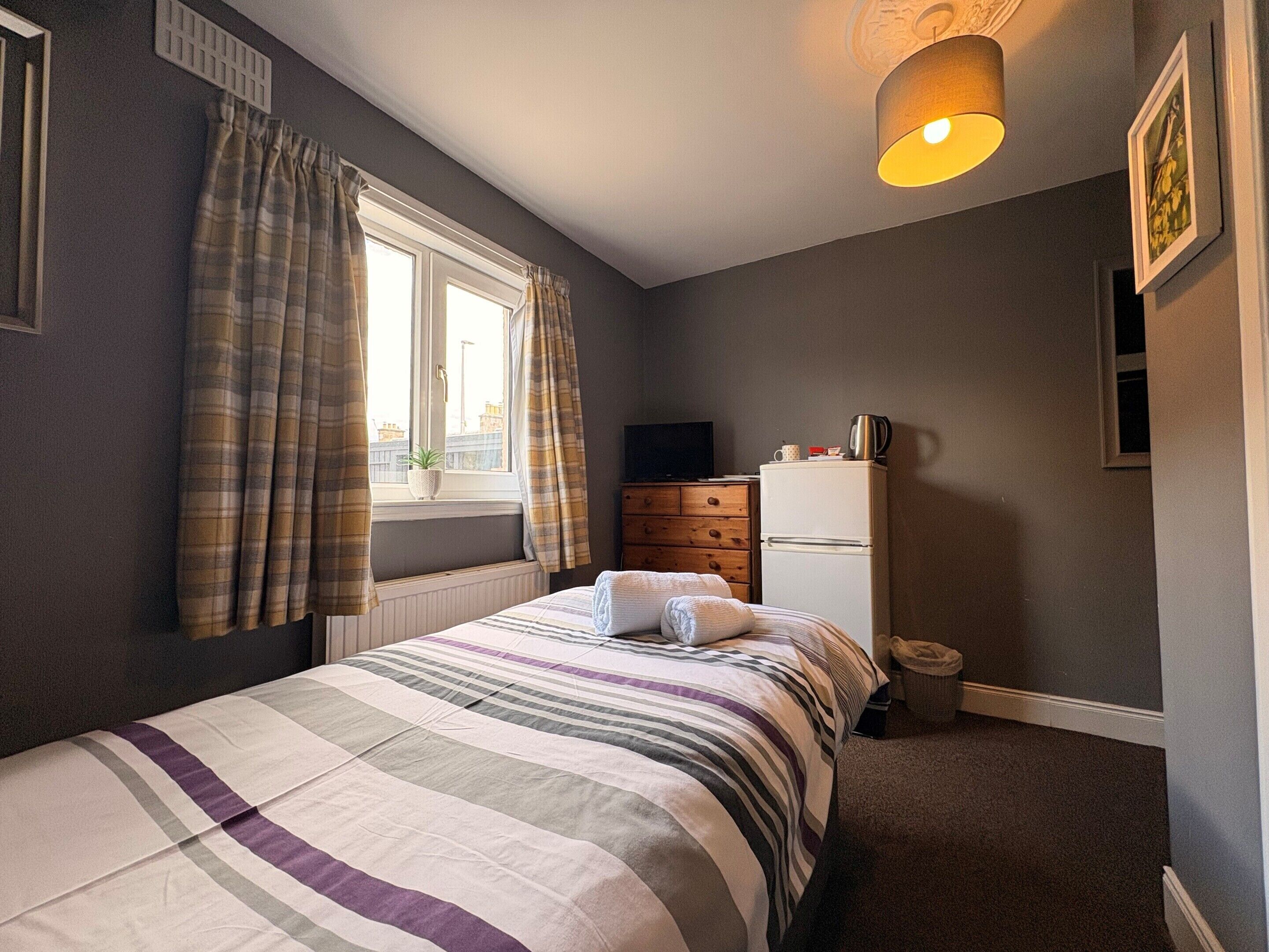 A bedroom with a bed, a dresser, a television, and a window with curtains.