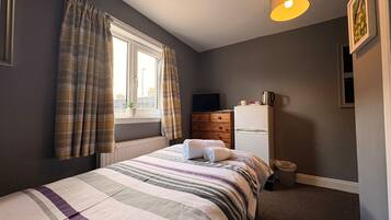 A bedroom with a bed, a dresser, a television, and a window with curtains.
