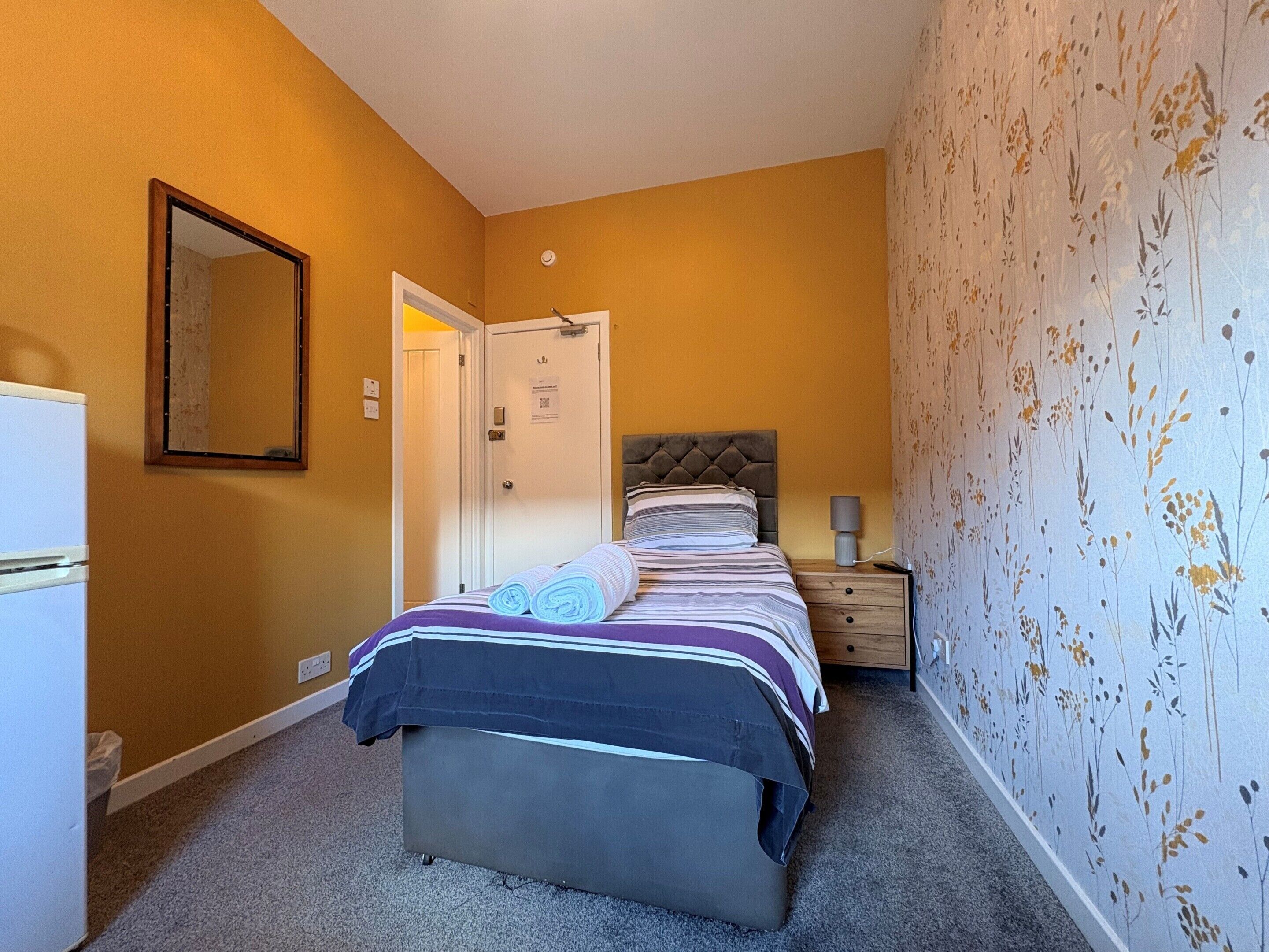 A bedroom with a bed, a nightstand, a mirror, and a door.