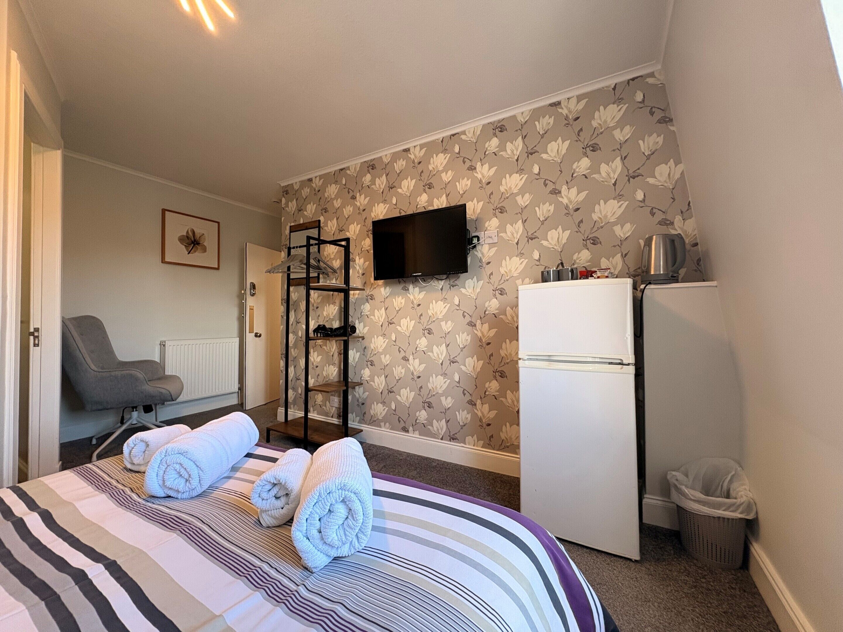 A hotel room with a bed, a chair, a TV, a refrigerator, and a trash bin.