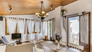 A cozy room with a wooden ceiling, a dining table with chairs, a sofa, a TV, and a fireplace.