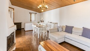 A living room with a wooden ceiling, a dining area with white furniture, and a sofa with patterned cushions.