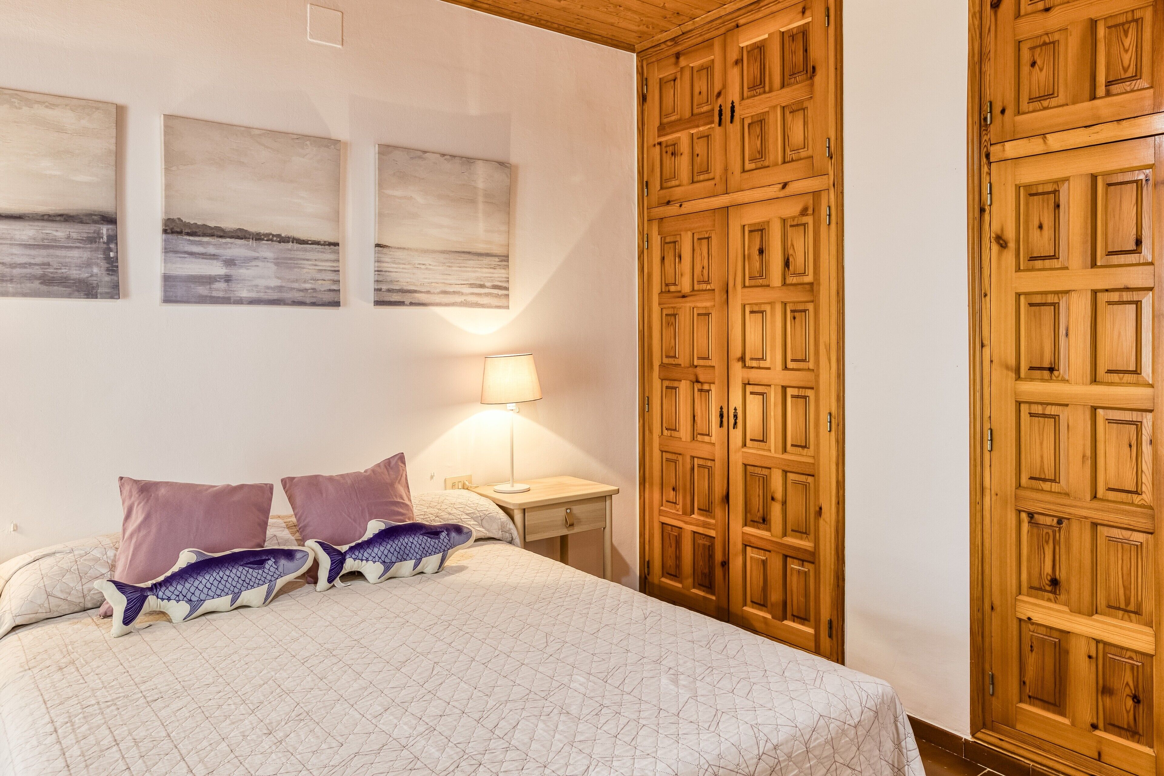 A bedroom with a bed, pillows, a nightstand, a lamp, and wooden wardrobe doors.