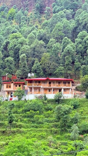A two-story building with balconies, surrounded by dense green forest.