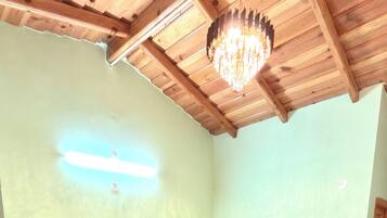 A bedroom with a wooden bed, a nightstand, a small table, a chandelier, and a wooden ceiling.