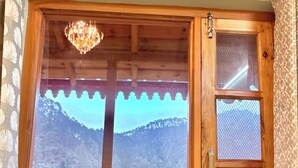 Una ventana con marco de madera, vista a un paisaje montañoso y un candelabro.