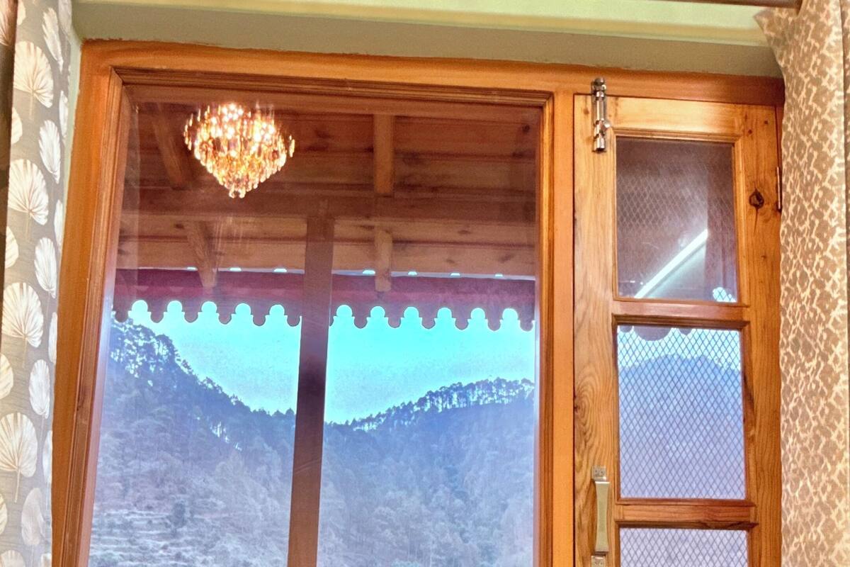 Una ventana con marco de madera, vista a un paisaje montañoso y un candelabro.