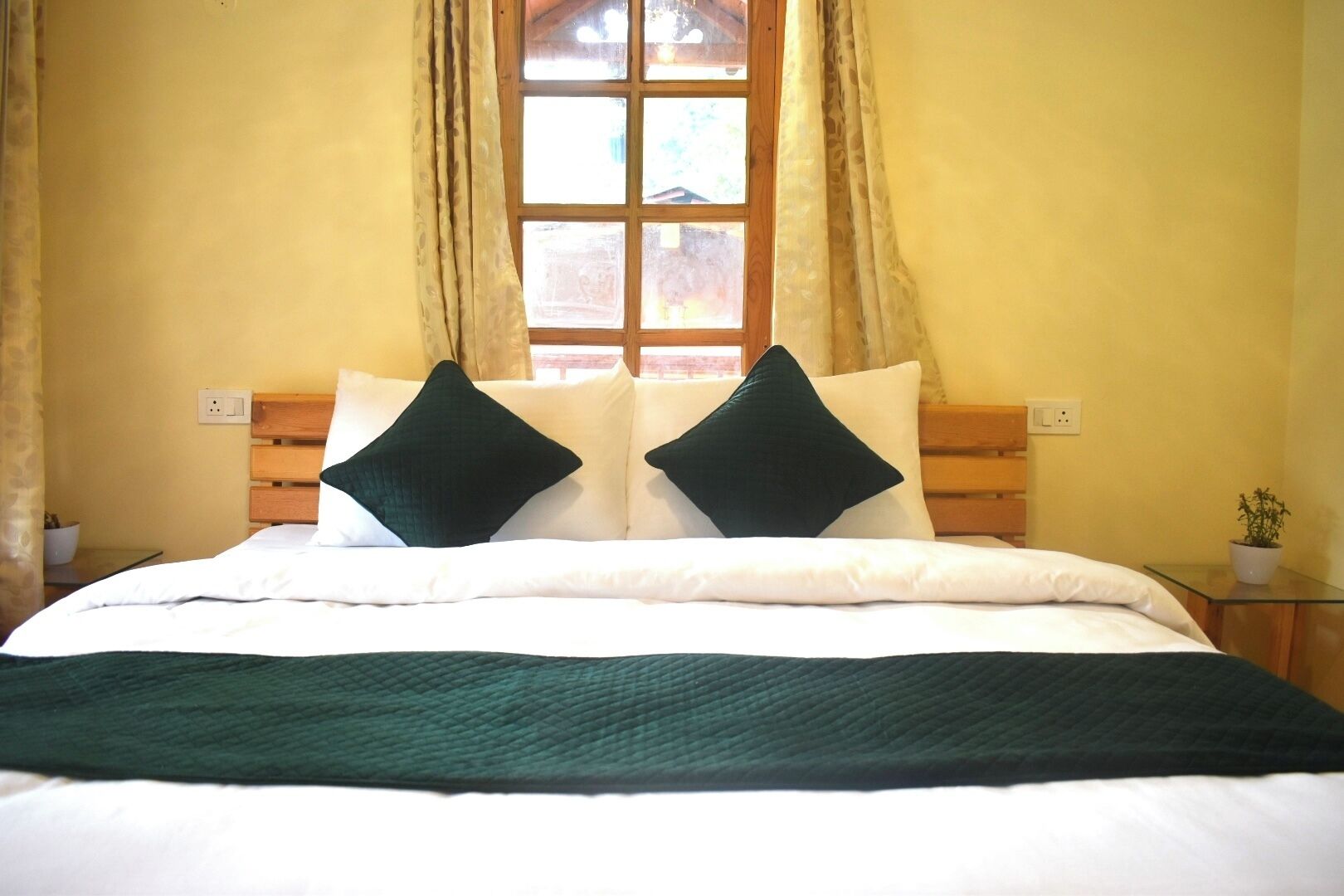 Un letto con poggiatesta in legno, due cuscini scuri, un piumone bianco e una coperta verde.