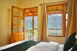 Ein Zimmer mit Bett, Fenster mit VorhĂ€ngen, Balkon mit GelĂ€nder und einer TĂŒr.