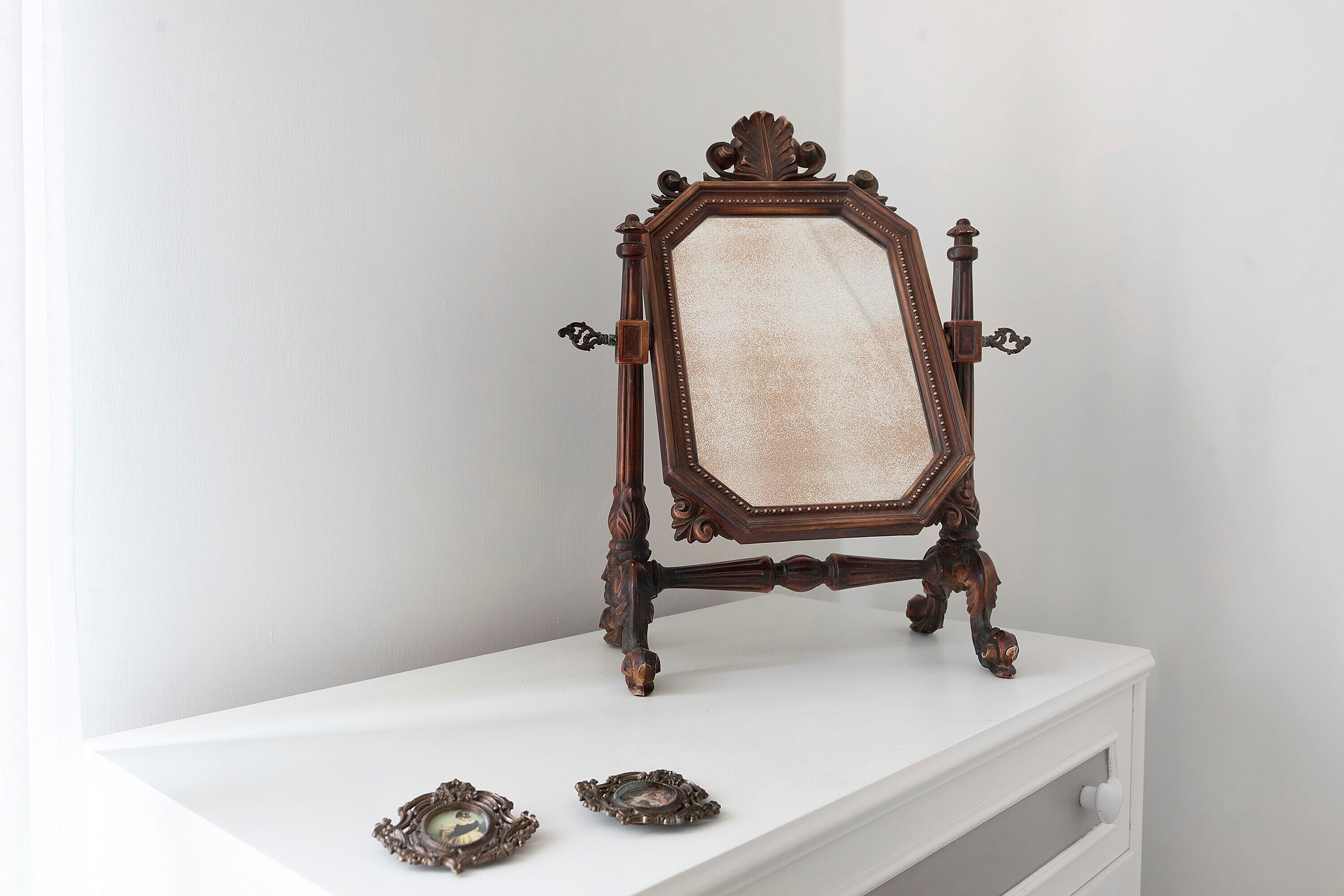 Un miroir avec un cadre orné, posé sur une commode blanche.