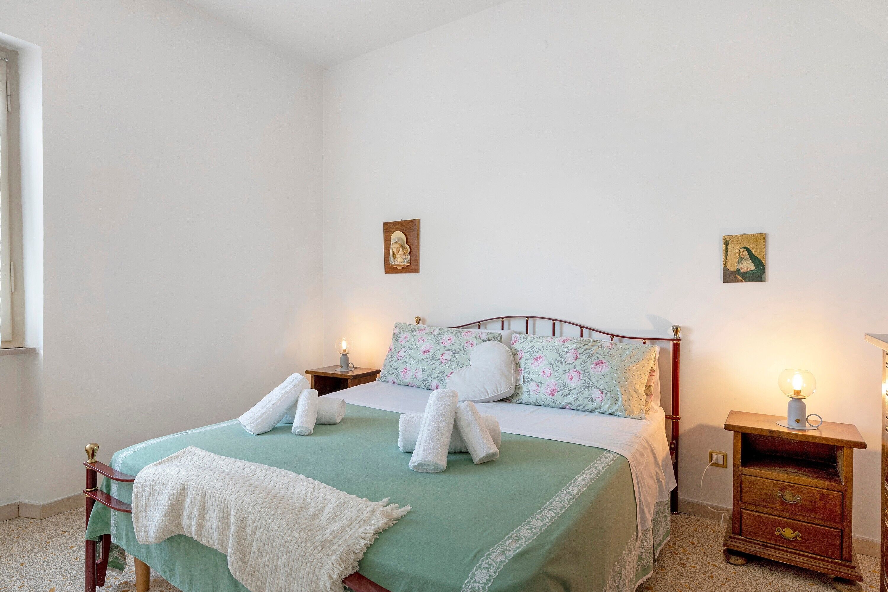 A bedroom with a bed, two bedside tables, a nightstand, and a window.
