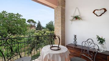 Een balkon met een tafel en stoelen, een hangplant en een decoratief object aan de muur.