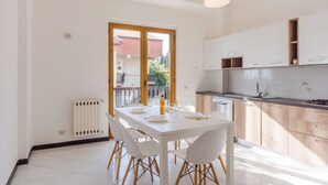 Una cuina moderna amb armaris blancs, una taula de menjador amb cadires i una vista per una porta de vidre.