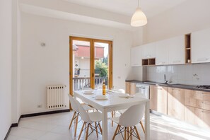 Uma cozinha moderna com armários brancos, uma mesa de jantar com cadeiras e vista através de uma porta de vidro.