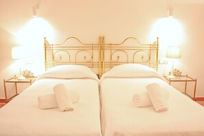 Un lit double avec une tête de lit dorée, deux tables de chevet avec des lampes et des serviettes pliées posées sur le lit.