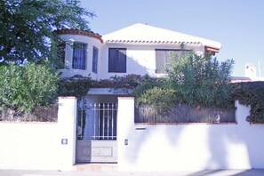 Un bâtiment blanc avec une entrée fermée par un portail, une enseigne portant le numéro 9 et, au fond, une petite structure ressemblant à une tour.