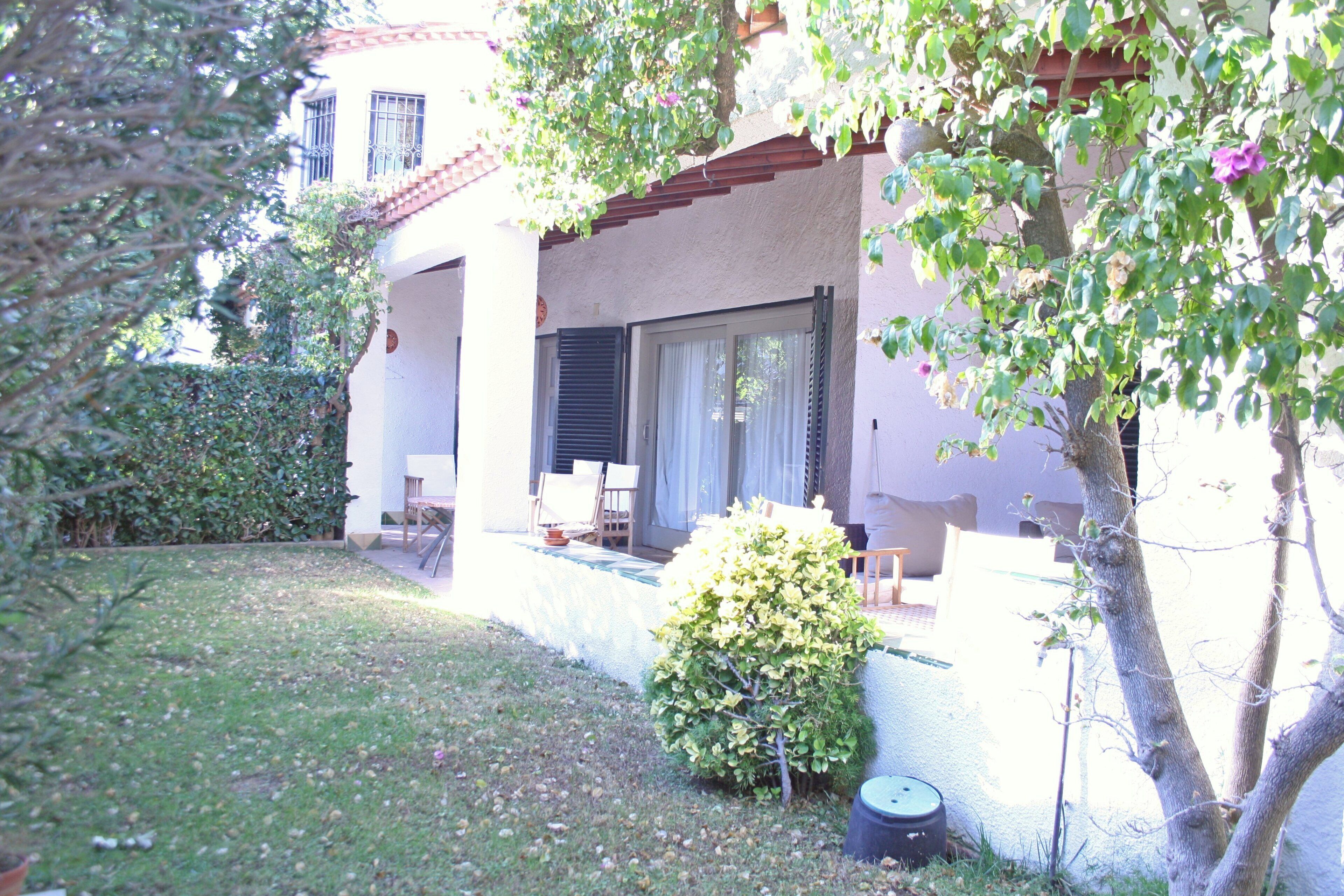 Une maison avec un patio, un petit jardin et un arbre.