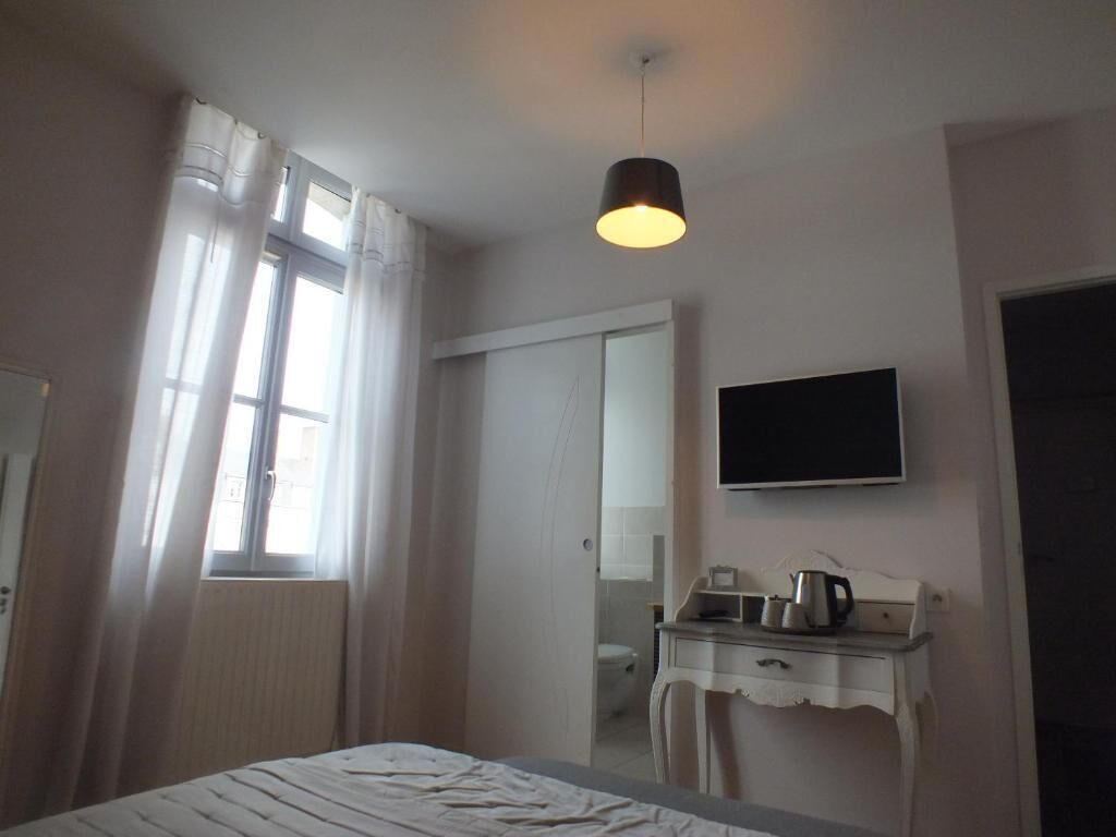 Un dormitorio con cama, una mesita de noche con hervidor, un televisor de pantalla plana, una ventana con cortinas y una puerta.