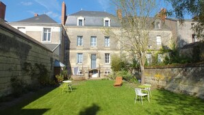 A courtyard with a lawn, a stone wall, and a building with multiple windows and a door. - La Fleur de Lys (Langeais)