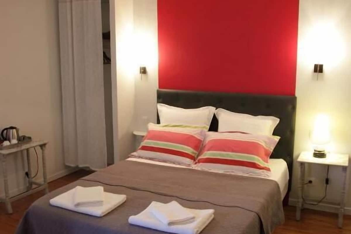 A hotel room with a bed, a nightstand, a lamp, and a red accent wall.