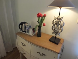 Un aparador de madera con un jarrón de tulipanes rojos, una lámpara y una bandeja con un hervidor y tazas.