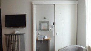 A room with a television, a cabinet, a chair, and a bathroom visible through an open door. - La Fleur de Lys (Langeais)