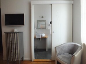 Habitació amb televisió, un armari, una cadira i un bany visible per una porta oberta.