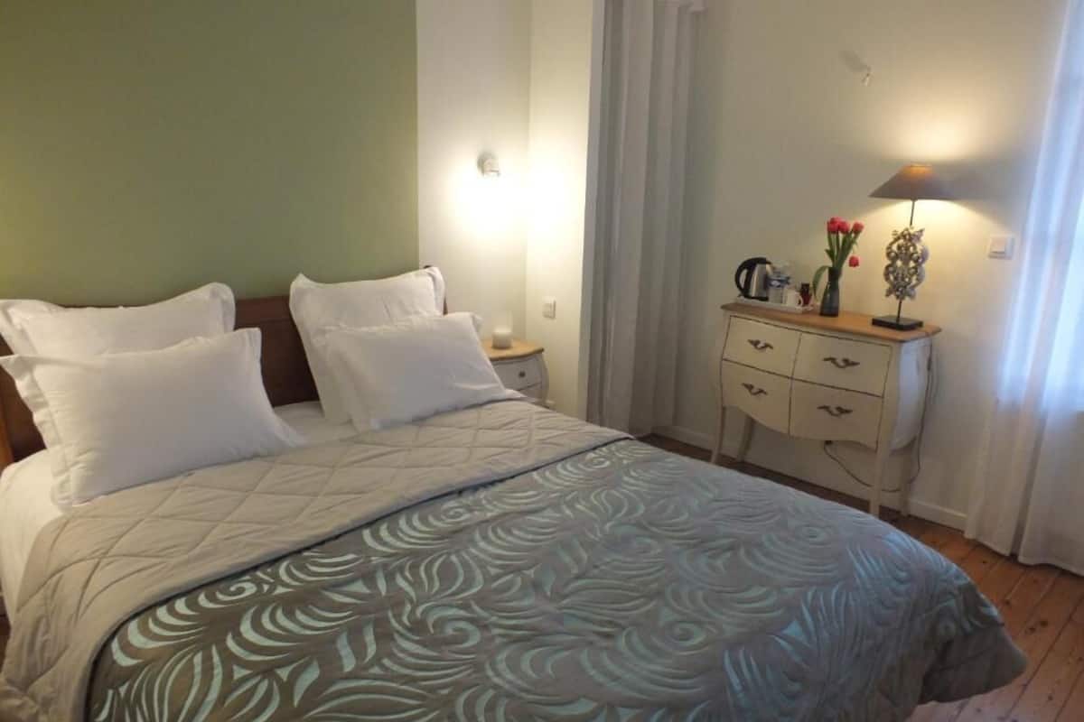 A neatly made bed with white linens, a bedside table with a lamp, and a dresser with drawers.