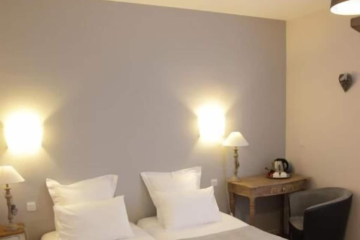A hotel room with a bed, two bedside tables, a chair, a lamp, and a wall-mounted light fixture.