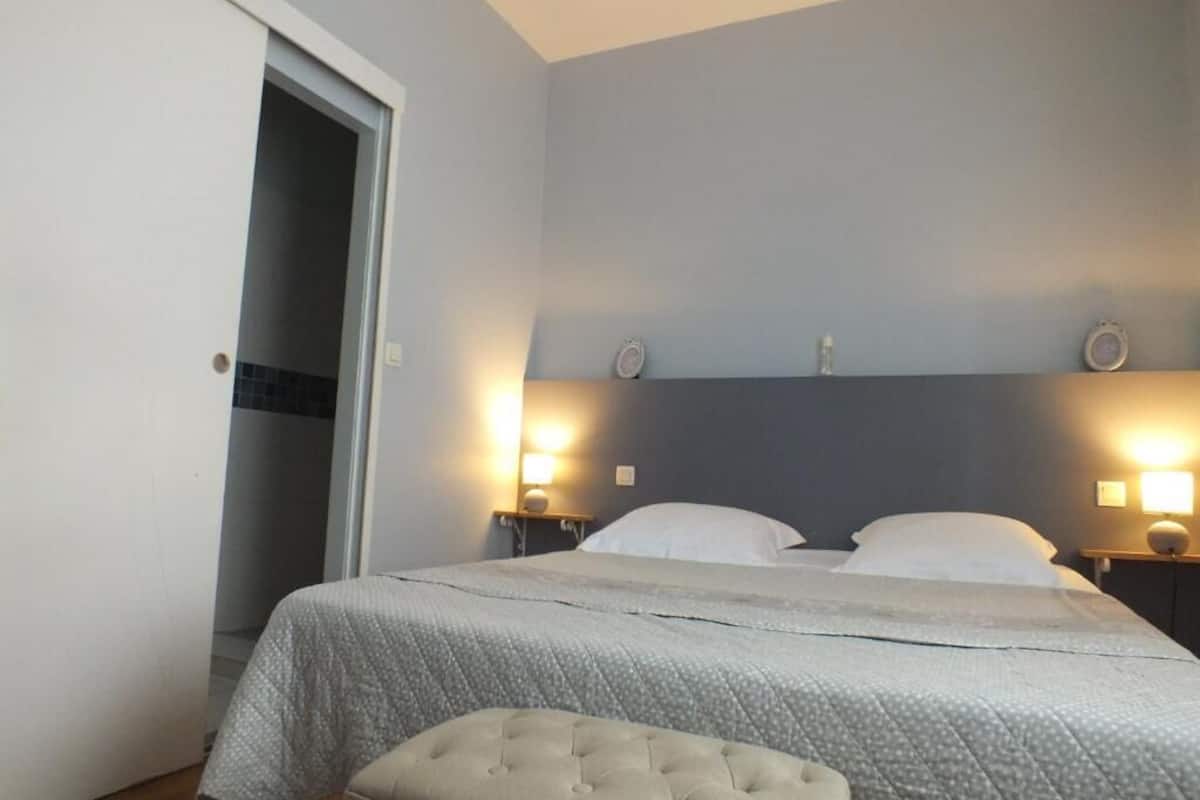 A bedroom with a bed, two bedside lamps, a nightstand, a door, and a wall-mounted light fixture.