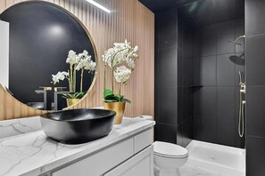 Un baño moderno con un espejo grande, un cuenco negro en la encimera, un inodoro y una zona de ducha.
