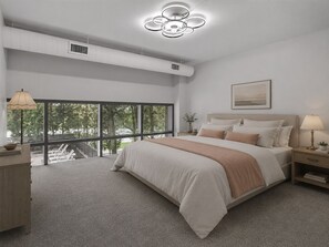 Un dormitorio con una cama grande, una mesita de noche, una lámpara, un ventilador de techo y una ventana con vistas a árboles.