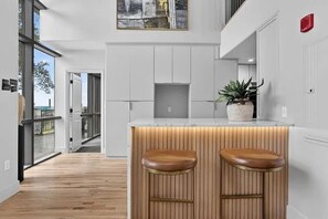 A modern kitchen with a central island, wooden stools, and a potted plant.